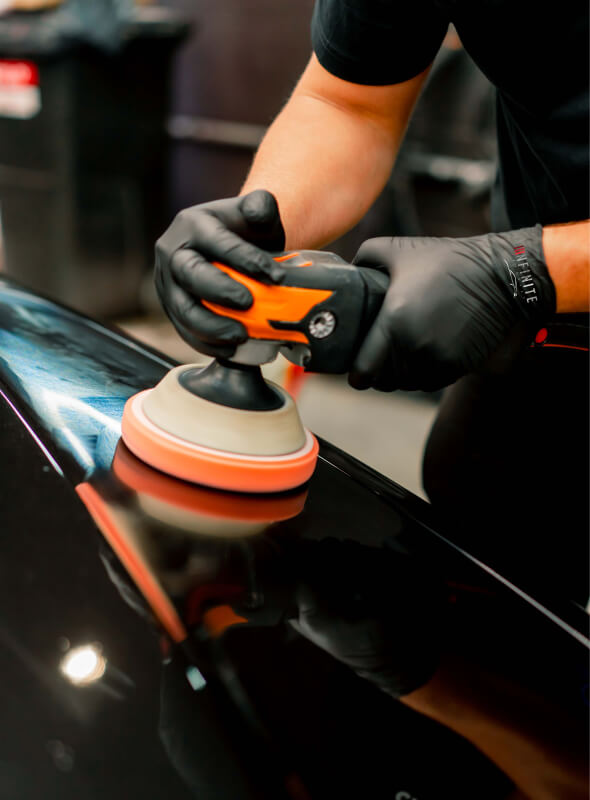 infinite autohaus person using a polisher to meticulously polish a sleek black car